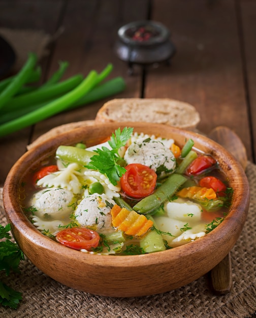 Dieta sopa de verduras con albóndigas de pollo y hierbas frescas en un tazón de madera