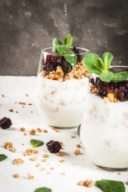 Dieta vegana desayuno saludable. Yogurt y granola con zarzamoras frescas y menta en un vaso. Sobre una mesa blanca. Copia espacio