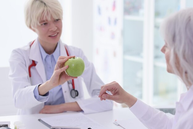 La dietista aconseja a la anciana que coma frutas frescas en el consultorio del hospital, la doctora da verde