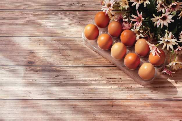 Diez huevos marrones y flores sobre fondo de madera. Concepto de vacaciones de Pascua. Estilo rústico. Plano, vista superior, espacio de copia.