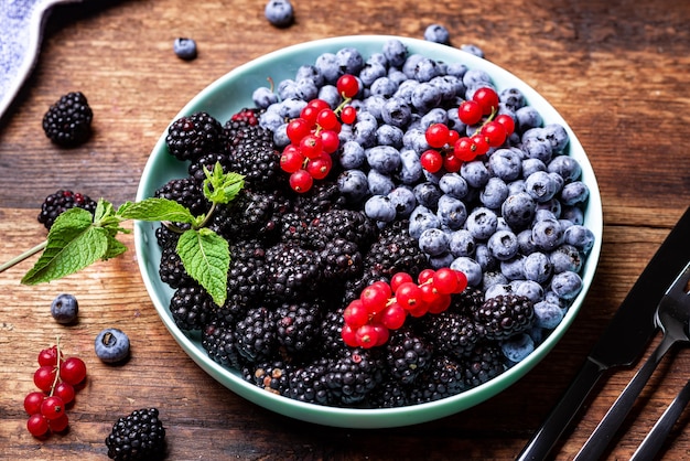 Diferente mezcla de bayas - arándanos, moras y grosellas rojas en un plato sobre un fondo de madera. Fondo de frutas, bayas.