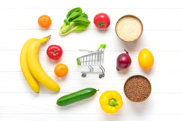 Diferentes alimentos saludables: trigo sarraceno, arroz, pimiento amarillo, tomates, plátanos, lechuga, verde, pepino, cebolla, carrito de compras