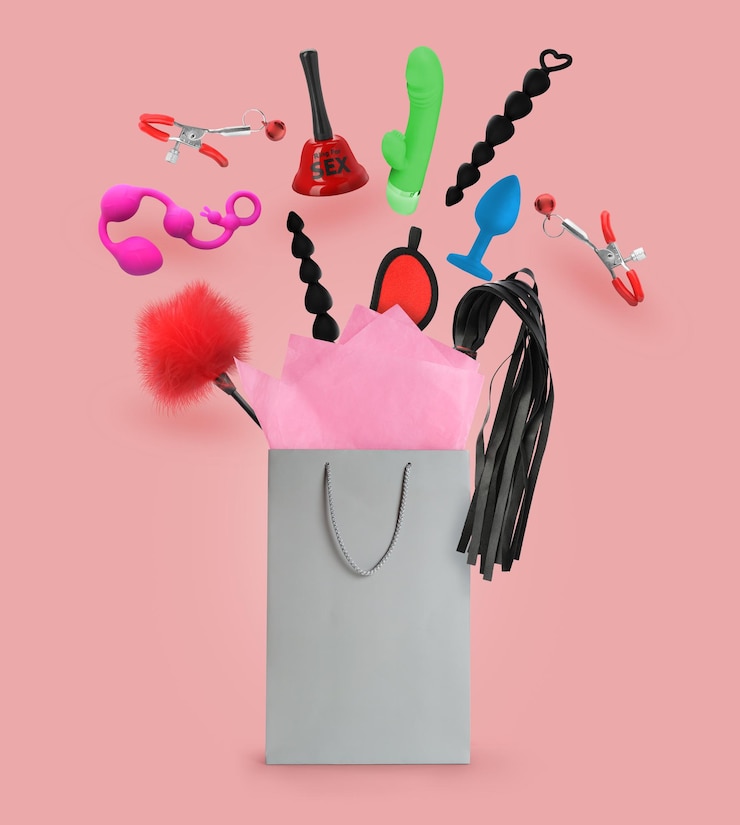 Foto diferentes brinquedos sexuais e acessórios caindo na sacola de papel no fundo rosa