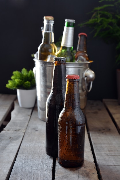 Diferentes cervezas en una mesa de madera. Hay botella y vaso con hielo para mantenerlos fríos.