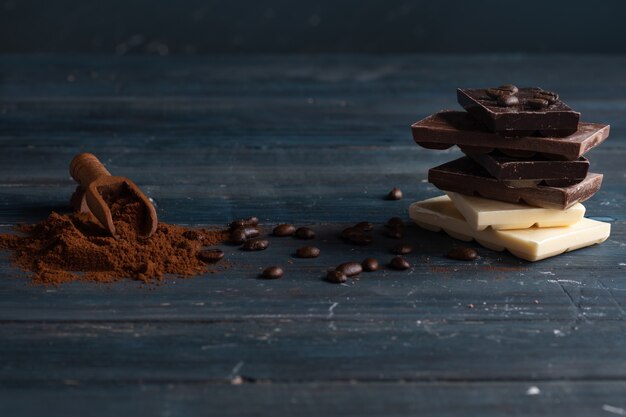 Diferentes chocolates, café en grano y café molido sobre fondo de madera