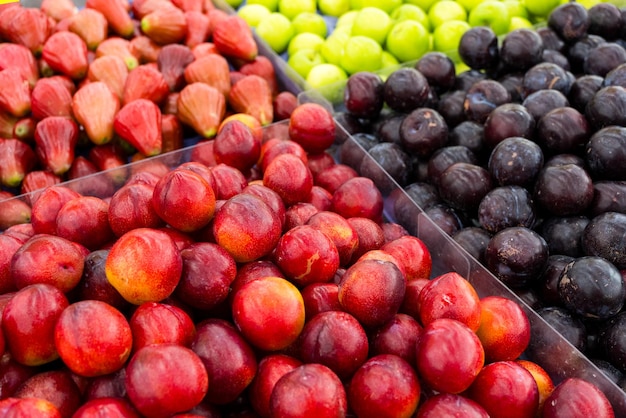 Diferentes ciruelas se venden en la tienda de frutas en el mercado