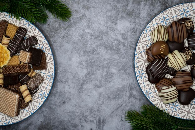 Diferentes doces de Natal, biscoitos de chocolate no prato e folhas perenes na mesa cinzenta.