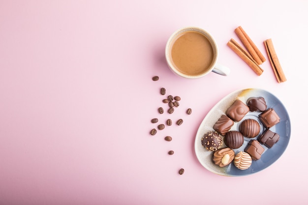 Diferentes dulces de chocolate y una taza de café sobre un fondo rosa pastel. Vista superior, espacio de copia.