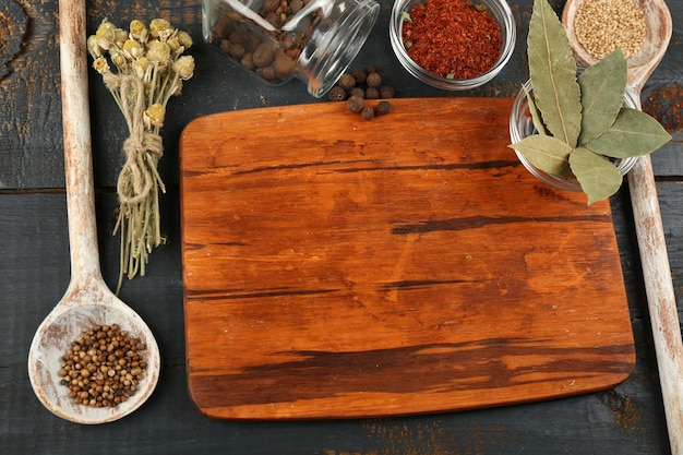 Diferentes especias y hierbas con tabla de cortar sobre fondo de mesa de madera de color