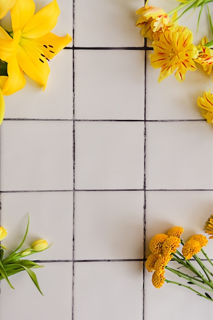 Diferentes flores amarillas sobre un fondo de piso de baldosas blancas