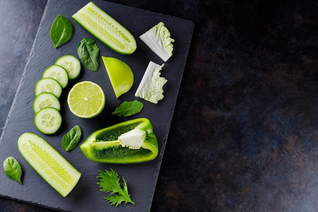 Diferentes frutas y verduras verdes sobre un fondo oscuro. Comida vegetariana saludable en una pizarra. Vista superior. Copia espacio