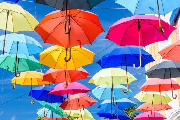 Diferentes guarda-chuvas coloridos pendurados na rua contra o céu azul