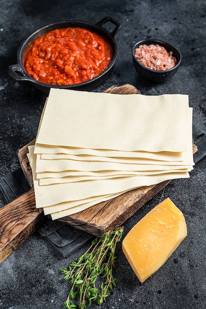 Diferentes ingredientes crudos para cocinar lasaña italiana en una mesa de cocina. Fondo negro. Vista superior.