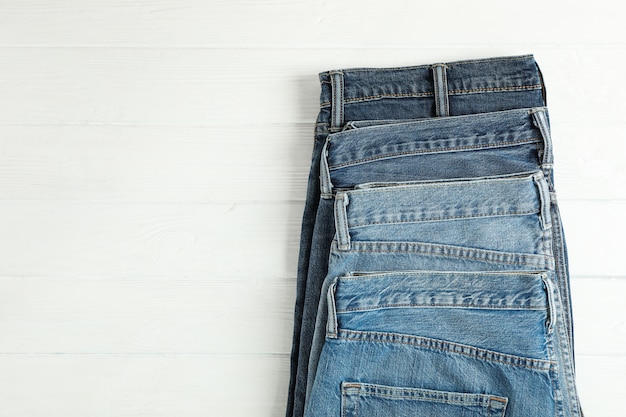 Diferentes jeans doblados sobre un fondo blanco de madera, espacio para texto