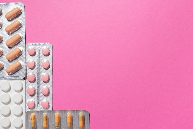Diferentes medicamentos, comprimidos, pílulas em blister, medicamentos medicamentos em fundo rosa. Fechar-se