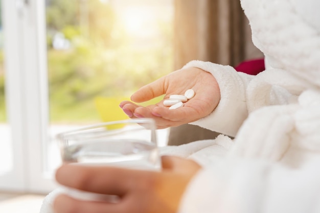diferentes pastillas blancas en la mano de una mujer joven con un vaso de agua