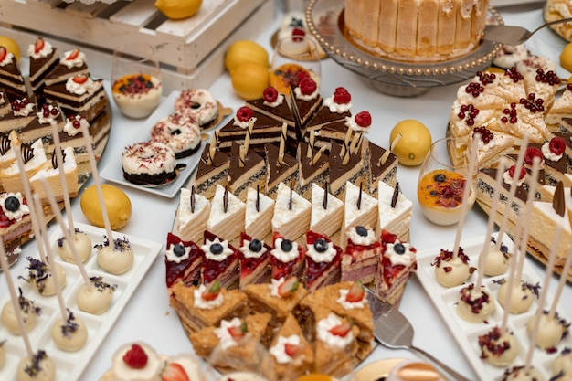 Diferentes piezas de deliciosos pasteles en una bandeja rodeada de frutas amarillas y canapés de postre wjite en el catering de bodas