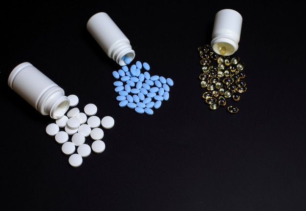 Diferentes píldoras médicas, tabletas y cápsulas sobre un fondo negro