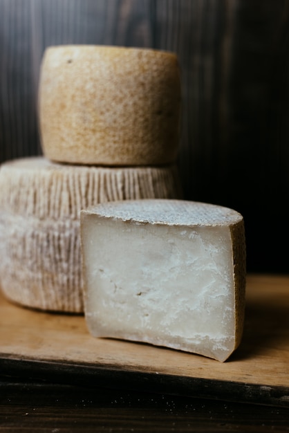 Diferentes quesos caseros en una mesa de madera oscura. Piezas y cabezas de queso de kravot, manchego, Paramezan. Queso de cabra y vaca sobre papel de horno. Trabajo manual. De cerca