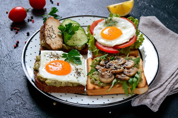 Diferentes sanduíches em uma mesa preta. Saboroso aperitivo saudável com abacate. Café da manhã rápido. Conceito de alimentação saudável. Nutrição apropriada