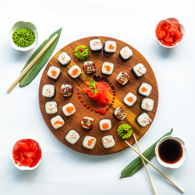 Diferentes sushi en una superficie redonda de madera con salsa de soja, jengibre, wasabi y palillos