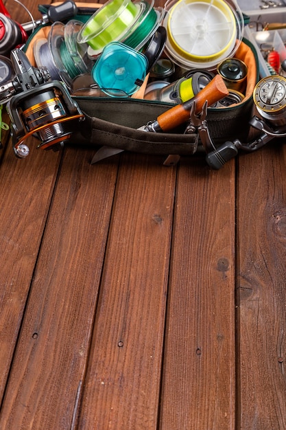 Diferentes tacos de pesca con señuelos y carretes sobre fondo marrón de madera con lugar para el texto. Diseño para publicidad y publicación.