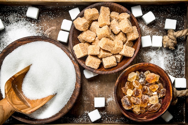 Diferentes tipos de azúcar en tazones en una bandeja sobre un fondo rústico