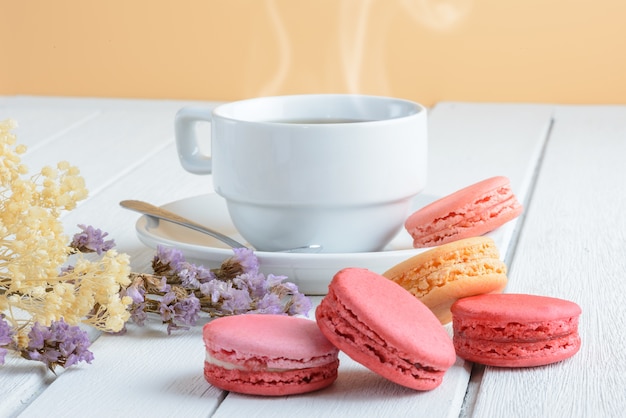 Diferentes tipos de color de macarrones con taza de té caliente en el fondo de madera blanca