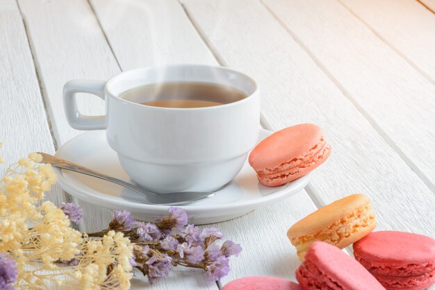 Diferentes tipos de colores de macarrones con taza de té caliente en la superficie de madera blanca