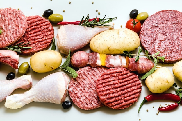 Diferentes tipos de carne crua: coxas de frango, hambúrgueres de porco e carne, costelas e kebabs, almôndegas de peru, prontas para serem cozidas com batatas, pimenta, azeitonas e azeitonas pretas e ervas aromáticas