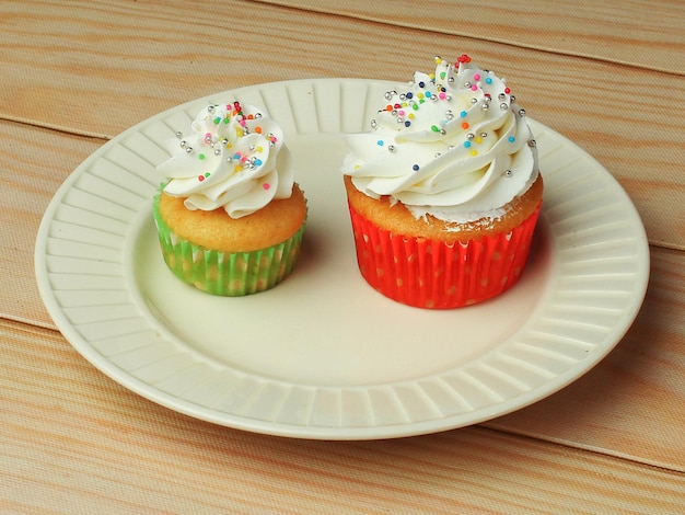 Foto diferentes tipos de cupcakes de baunilha com cobertura de creme de manteiga branca e granulado na chapa branca para festa de aniversário