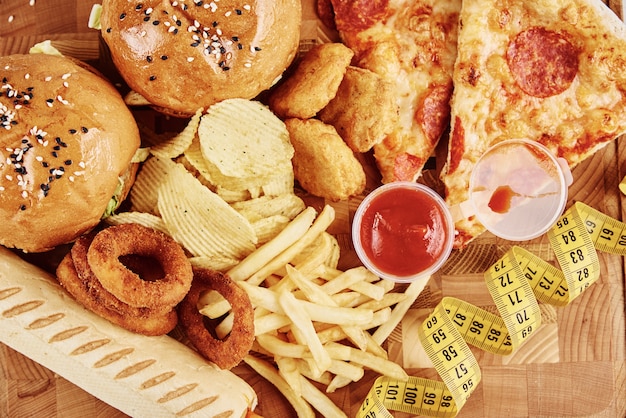 Foto diferentes tipos de fastfood e lanches na mesa com fita métrica