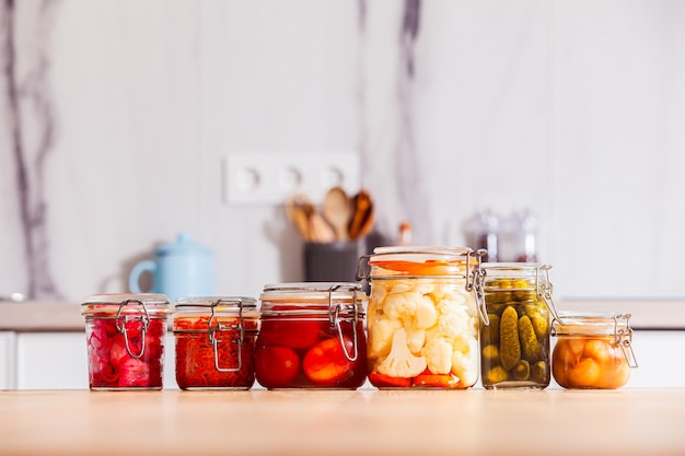 Diferentes tipos de legumes em conserva dispostos em uma linha em uma mesa na cozinha