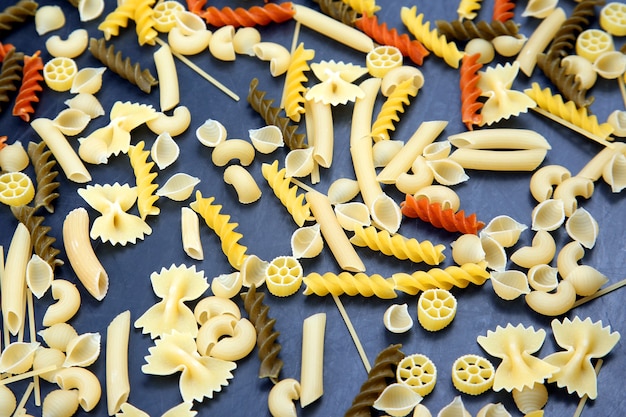 Foto diferentes tipos de massas italianas coloridas em um fundo escuro. textura de comida. produtos de farinha e alimentos na culinária