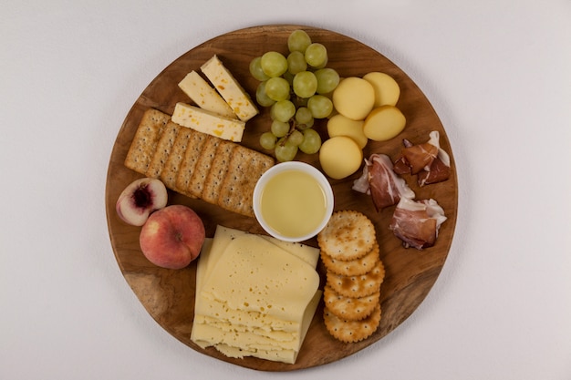 Diferentes tipos de queijo, biscoitos crocantes, frutas e molho na placa de madeira