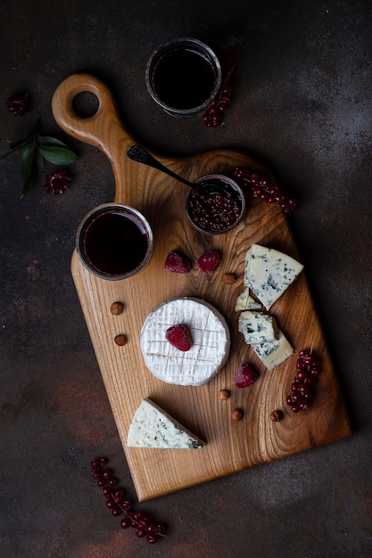 Diferentes tipos de queijo na tábua de madeira com frutas e vinho
