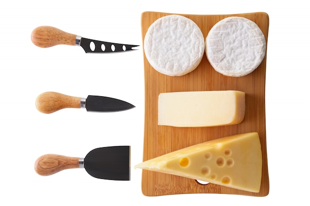 Diferentes tipos de queijos - brie, camembert, queijo parmesão e gouda na placa de madeira com facas de queijo isolado no branco