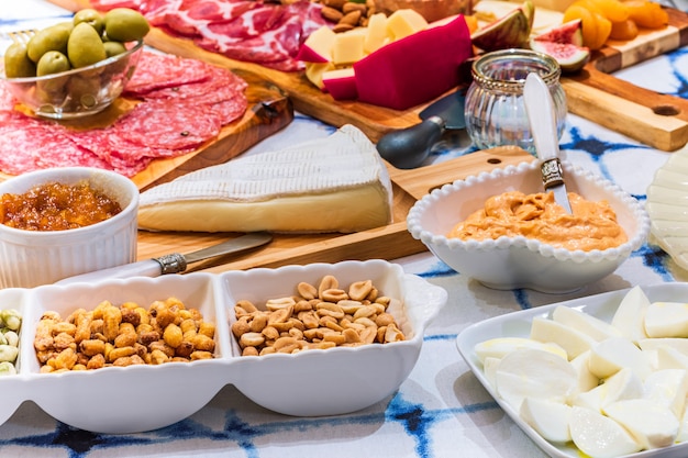 Diferentes tipos de queijos, vinhos, baguetes, frutas e petiscos à mesa para degustação e cenário de férias.