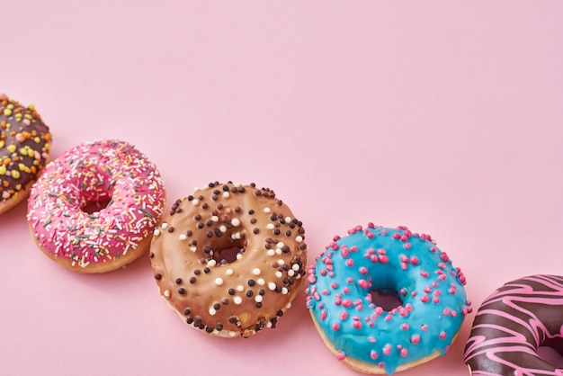 Diferentes tipos de donas de colores decoraron chispas y glaseados sobre una superficie rosa pastel