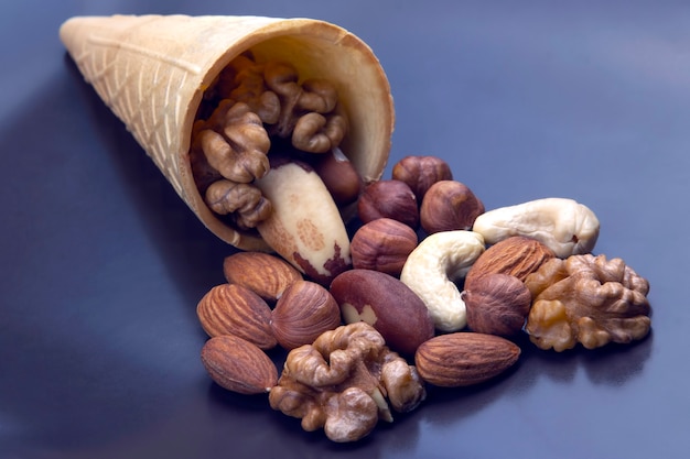 Diferentes tipos de nueces en un cono de galleta sobre una superficie gris. Alimentos saludables y proteicos