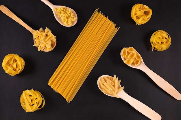 Diferentes tipos de pasta en cucharas de madera sobre mesa negra