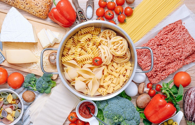 Diferentes tipos de pasta italiana sobre un fondo de madera con varios ingredientes para cocinar platos tradicionales italianos