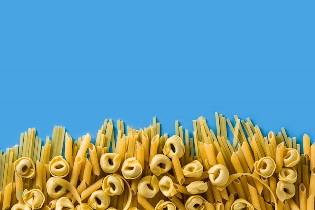 Diferentes tipos de pasta Ravioli penne pasta tortellini y capellini sobre fondo azul.