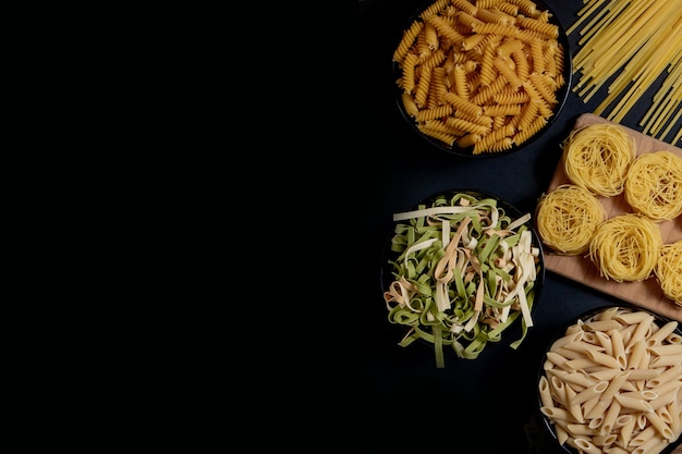 Foto diferentes tipos de pasta seca en el plato y en cuencos sobre fondo negro. espacio para texto, vista superior