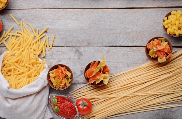 Diferentes tipos de pasta y tomates sobre fondo de madera