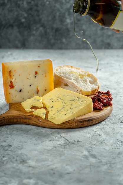 Diferentes tipos de queso en tabla de cortar de madera. queso azul con chapata y tomates secados al sol sobre fondo gris. Cena de cocina italiana. vierta aceite de girasol en el pan. Enfoque suave, de cerca