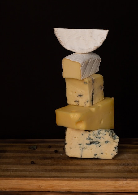 Foto diferentes tipos de queso en una tabla de cortar de madera rústica sobre un fondo oscuro. vertical. copie el espacio.