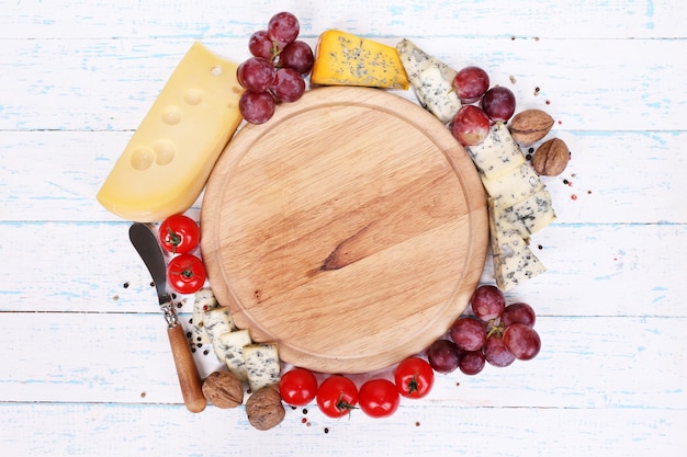 Foto diferentes tipos de queso con tablero vacío en primer plano de la mesa