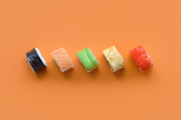 Diferentes tipos de rollos de sushi asiáticos sobre fondo naranja Minimalismo vista superior plana con comida japonesa