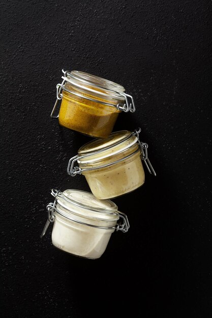 Foto diferentes tipos de salsas en frascos de vidrio con anacardos de pistachos y mayonesa vegana sobre fondo negro